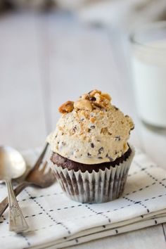 a cupcake on a napkin with a spoon and glass of milk in the background