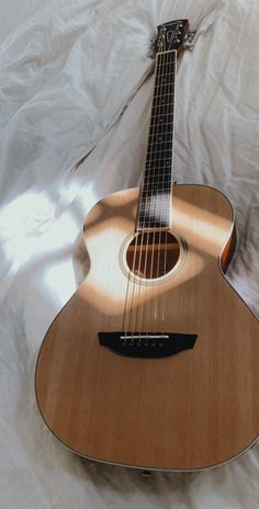 an acoustic guitar laying on top of a white sheet covered bed with the strings still attached