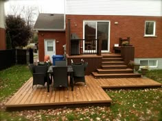 a deck with chairs and table in front of a brick house on the grass outside