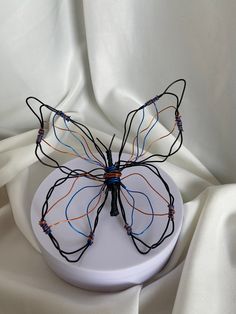 a wire butterfly sculpture sitting on top of a white plate with wires attached to it