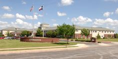 an american flag flies in front of the school building with cars parked on the street