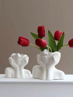 two white vases with red tulips in them on a shelf next to each other