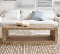 a coffee table with two candles on it in front of a white couch and three framed pictures