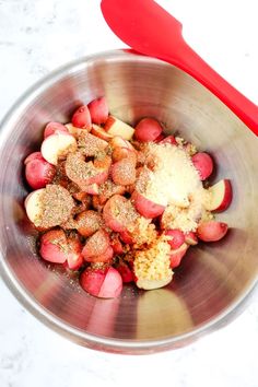 a metal bowl filled with food next to a red spatula on top of a white counter