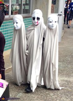 three people in white masks standing next to each other on the side of a street