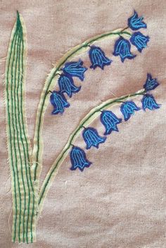 some blue flowers are on a piece of cloth with green thread and stitching around the edges