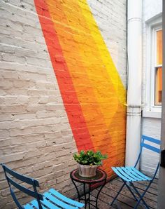 a rainbow painted on the side of a building with two chairs and a small table