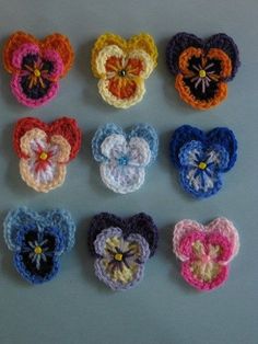 six crocheted hearts arranged in different colors and sizes on a gray surface,