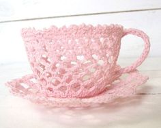 a pink crocheted cup and saucer on a white table