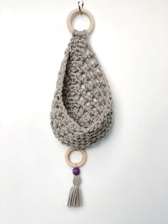 a crocheted purse hanging from a hook on a white wall with a wooden ring