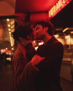 a man and woman kissing in front of a neon sign