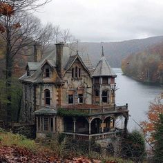 an old house sitting on top of a hill next to a lake in the woods