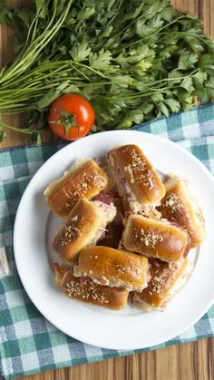 small sandwiches on a white plate next to tomatoes and parsley