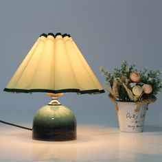 a green lamp sitting on top of a table next to a pot with flowers in it