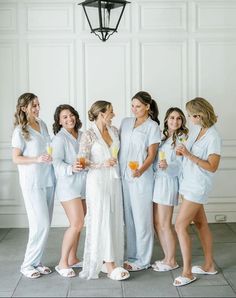 a group of women standing next to each other in white robes and holding drinks together