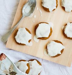 a wooden cutting board topped with frosted cupcakes next to a tea pot