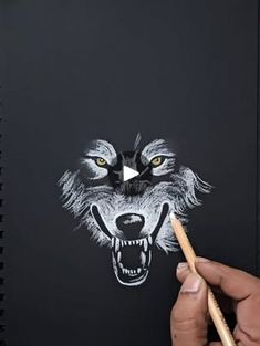 someone is drawing a wolf's face on a notebook with pencils and paper