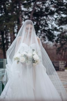 a woman in a wedding dress with a veil over her head and flowers on her bouquet