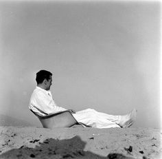 a man sitting on the beach with his legs spread out and looking off into the distance