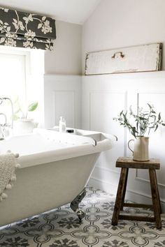 a white bath tub sitting under a window next to a wooden stool with flowers on it