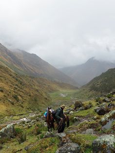 two people are riding horses on a rocky trail in the middle of a mountain range