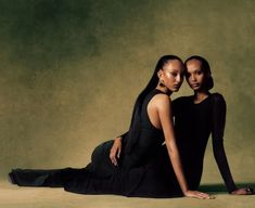 two women are sitting on the ground posing for a photo together, one is wearing a black dress