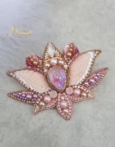 a brooch with pink and white pearls on it's center, surrounded by feathers