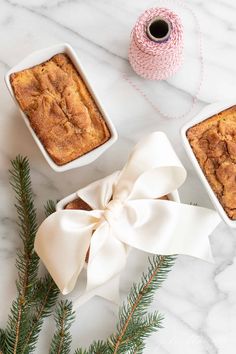 two white dishes filled with baked goods next to a sprig of pine