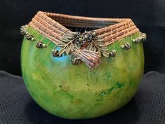 a close up of a green vase on a black surface with beads and leaves attached to it