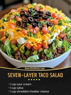 the seven layer taco salad is served in a bowl with cheese and olives