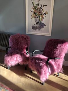 two purple chairs sitting next to each other in front of a painting on the wall