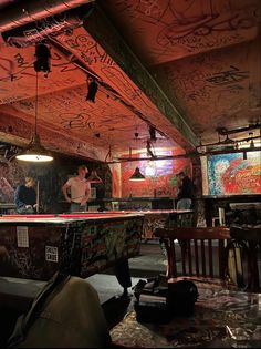 a man standing in front of a pool table covered in graffiti on the walls and ceiling