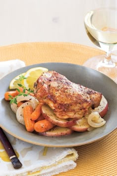 a plate with chicken, carrots and potatoes on it next to a glass of wine