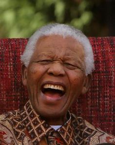 an older man laughing while sitting in a chair with his eyes closed and mouth wide open