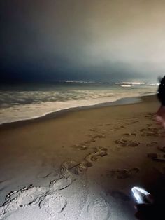 a person is walking on the beach with their cell phone in hand and footprints in the sand