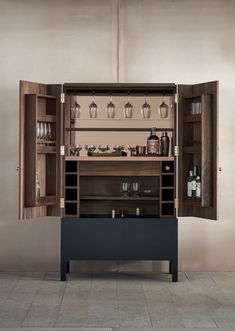 an open cabinet with wine glasses and bottles on it, in front of a wall