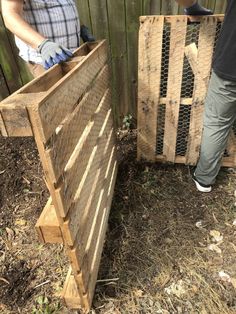 two men are working on some wood in the yard, one is holding a chicken cage and the other is standing next to a fence