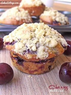 blueberry muffins with crumbled topping sitting on a table next to fresh cherries