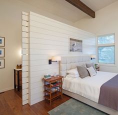 a bed sitting in a bedroom next to a window with white walls and wood floors