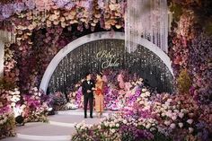 two people standing in front of a floral display at a fashion show with purple and pink flowers