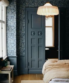 a bedroom with blue wallpaper and wooden flooring next to a large bed in front of a black door