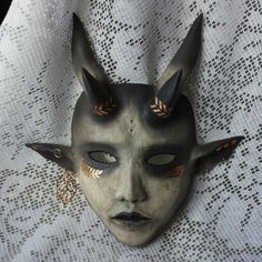 a black mask with horns and leaves on it's face sitting on a lace tablecloth