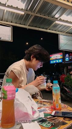 a young man sitting at a table with drinks in front of him and looking at his cell phone