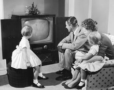 an old black and white photo of three children watching tv with their mother sitting on the couch