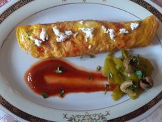 an omelet is on a plate with some vegetables and sauce next to it