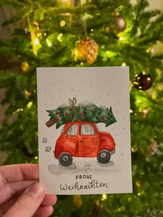 a hand holding up a card with a red car carrying a christmas tree on top