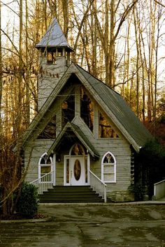 an old church with a steeple and white door is shown in front of some trees