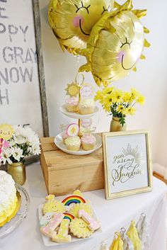 a table topped with cupcakes, cookies and balloons