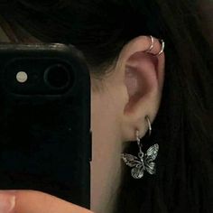 a woman taking a selfie with her cell phone while wearing butterfly earrings