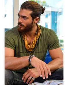 a man with a beard sitting on a blue couch looking off to the side while wearing a necklace